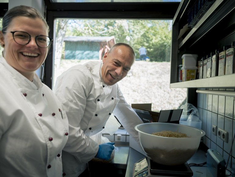 Ein Mann und eine Frau stehen lachend in der Küche und haben Spaß an ihrer Arbeit.