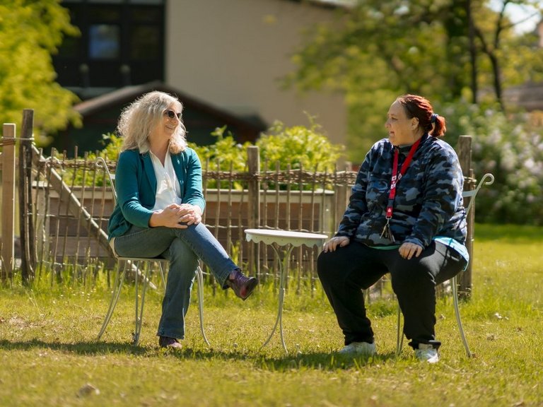 Zwei Frauen sitzen sich im Garten gegenüber und tauschen sich aus.