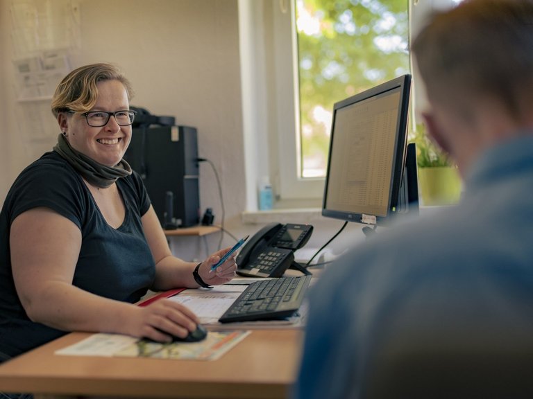 Zwei Person sitzen vor einem PC und unterhalten sich. 