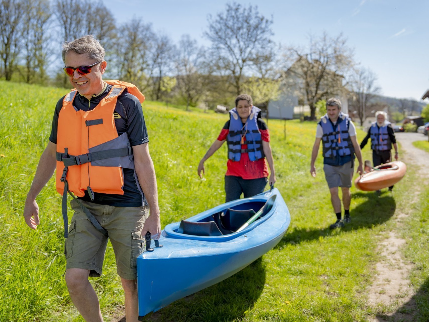 Vier Personen auf dem Weg zum Kanufahren, gemeinsames Tragen.